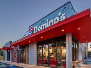 Fachada de una tienda de Domino’s Pizza con el logotipo visible y zona de comedor exterior
