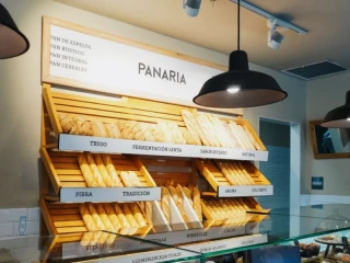 Interior de una panadería de la franquicia Panaria con exposición de panes artesanales y cartel corporativo.