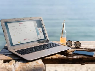 Ordenador portátil en la playa junto a bebida y gafas de sol, símbolo del trabajo y crecimiento de franquicias en verano en España