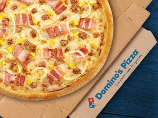Pizza de Domino’s Pizza sobre caja de cartón con logo y lema de la marca, imagen promocional de la franquicia Domino’s Pizza.