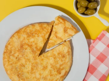 Tortilla de patatas casera recién hecha en plato blanco con aceitunas verdes de acompañamiento