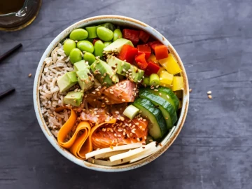 Poke bowl con arroz integral, salmón fresco, aguacate, edamame, pepino, pimientos y zanahoria, decorado con semillas de sésamo
