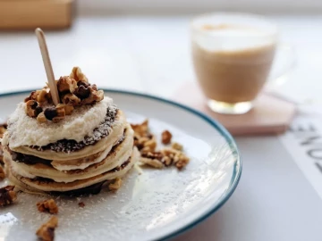 Plato de pancakes artesanales con nueces y nata acompañado de café en una cafetería
